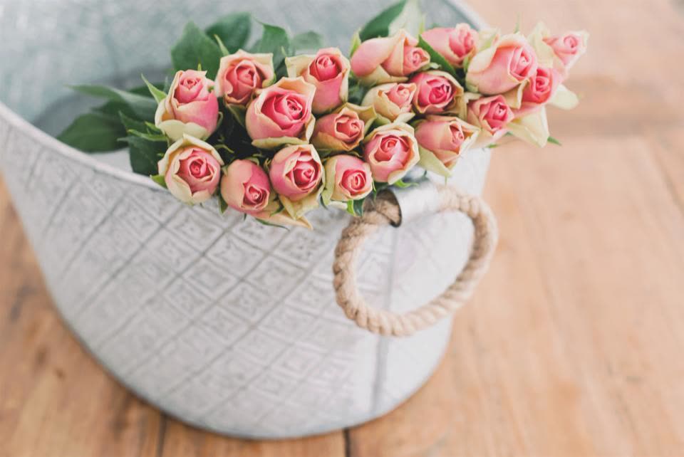 Pink roses and green leaves in a grey woven basket